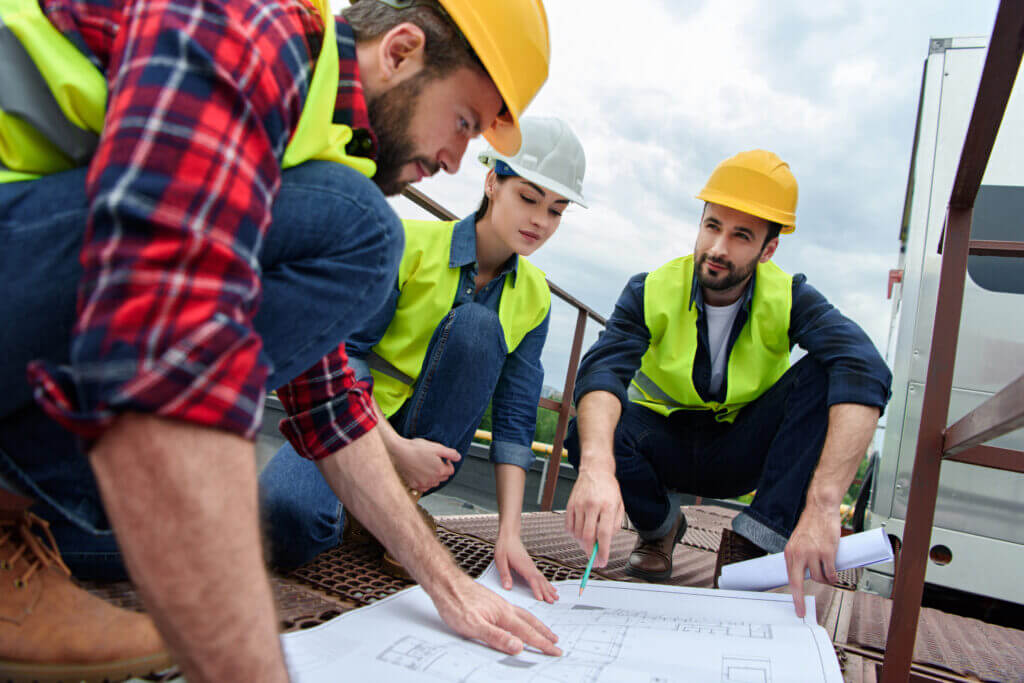 three engineers in hardhats working with blueprints on roof | earthingequip.com